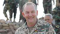 Die Freude an seiner Tätigkeit im Einsatz sieht man dem Chef der deutschen Kräfte im Irak und Kuwait deutlich an Ein deutscher Oberst geht lächelnd vor anderen Soldaten entlang