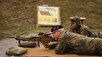 Ein Soldat visiert mit dem Maschinengewehr am Boden liegend das Ziel an, ein zweiter assistiert ihm.