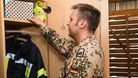 Ein Soldat steht vor seinem offenen Spint und hält eine bunte Box