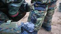 Zwei Soldaten mit ABC-Schutzanzug helfen sich gegenseitig beim anziehen