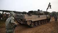 Zwei Soldaten in Schutzanzügen spritzen einen Panzer ab
