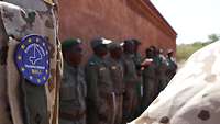 Im Vordergrund: das Wappen der EUTM in Mali. Im Hintergrund: angetretene malische Soldaten des Ausbildungsdurchgangs