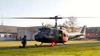 Ein Hubschrauber steht auf einer Wiese, der Einweiser für den Landeplatz kniet davor.