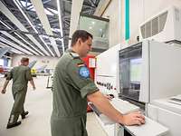 Dokumentieren der Arbeitsschritte Ein Soldat steht vor einem Computer während ein anderer im Hintergrund weggeht