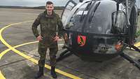 Ein Soldat im Feldanzug steht auf dem Flugfeld vor einem Hubschrauber.