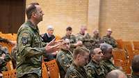 Mehrere Soldaten sitzen in einem Saal, ein Soldat steht und stellt eine Frage an den Redner.