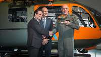 Zwei Zivilisten und ein Soldat stehen vor einem Hubschrauber und lächeln, zwei schütteln ihre Hände.