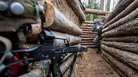 Bewaffnete Soldaten kämpfen in einer mit Baumstämmen befestigten Stellung.