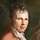 Alexander von Humboldt Porträt Porträtbild eines sitzenden Mannes in weißem Hemd und hellroter Weste, in den Händen eine Blume und ein Buch