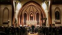 Mehrere Menschen sitzen nebeneinander auf Sitzbänken in der Kirche Warnemünde.