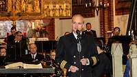Ein Mann in Marine-Offizieruniform steht vor einem Mikrofon.