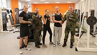 Fünf Soldaten, teils in Sportkleidung und in Uniform, stehen zum Gruppenfoto im Fitnessraum.