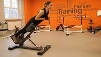 Eine Soldatin in Sportkleidung trainiert auf einem Fitnessgerät die Rückenmuskulatur.