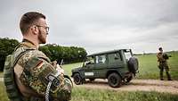 Im Vordergrund Oberfeldwebel Riedel mit seinem Funkgerät. Im Hintergrund ein Fahrzeug und ein Soldat seiner Gruppe.