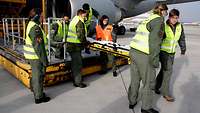 Soldaten in Uniform und Signalweste heben eine leere Trage vom heruntergefahrenen Highloader.