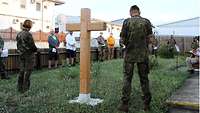 Militärpfarrerin Barbara Reichert und Kontingentführer Oberst Volker Eden stehen neben einem Holzkreuz beim Gebet