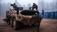 Zwei Soldaten öffnen die Motorhaube eines Gefechtsfahrzeuges.