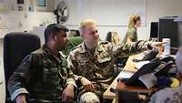 Zwei Soldaten sitzen an einem Computer, im Hintergrund sieht man eine Soldatin