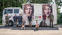 Sechs Personen stehen und zwei Personen knien vor einem Lastkraftwagen des Deutschen Roten Kreuzes