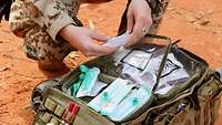 Ein Soldat kniet vor seinem geöffneten Sanitätsrucksack und hat eine medizinische Lösung in der Hand