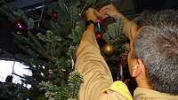 Ein Soldat hängt eine Christbaumkugel an einen Tannenbaum