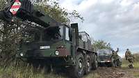 Ein Kranfahrzeug und ein Militärlastwagen stehen hintereinander.