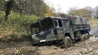 Ein großer Militärlastwagen hat sich in einem Waldstück im schlammigen Untergrund festgefahren.