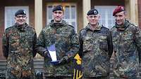 Vier Soldaten stehen nebeneinander. Ein Soldat hält einen Pokal in der Hand. 