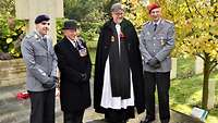 Zwei deutsche Soldaten stehen mit einem britischen Pfarrer und einem Zivilisten vor einem Steinkreuz
