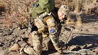 Ein Soldat kniet vor einem abgespannten Seil und überprüft die Befestigung auf eventuelle Schäden.