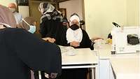 Mehrere Frauen mit Kopftuch und Maske sortieren und verpacken Masken 