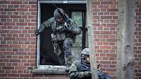 Ein Soldat steht vor einem Fenster und beobachtet die Umgebung, ein zweiter springt aus dem Fenster.