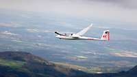 Ein Segelflugzeug fliegt über eine hügelige Landschaft.