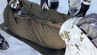 Der gerettete Soldat wird geschützt mit einem Schlafsack und einer isolierenden Matte vor dem Erfrieren geschützt.