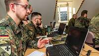 Mehrere Soldaten sitzen vor ihren Laptops in einem Unterrichtsraum mit schrägem Dach.