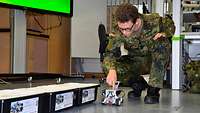 Jugendlicher in Flecktarn bedient einen kleinen Roboter.