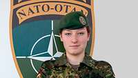 Eine Soldatin steht vor dem Wappen der Enhanced Forward Battle Group