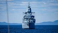 Frontal view of the frigate at sea, coastline in the background