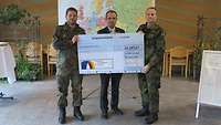 Zwei Soldaten mit einem großen Scheck vor einer Europakarte, in der Mitte ein Zivilist.