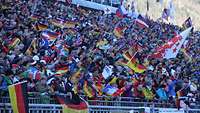 Voll besetzte Fan-Tribüne im Freien mit vielen Deutschland-Fahnen.