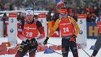 Mehrere Biathleten fahren an einer Bande vorbei.