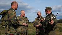 Vier Soldaten stehen im freien Gelände und unterhalten sich.