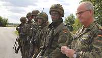 Fünf Soldaten stehen ausgerüstet und mit Tarnfarbe in einer Reihe, rechts ein General in Flecktarn.