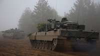 Zwei deutsche Kampfpanzer sind auf sandigem Boden unterwegs. Es ist sehr neblig