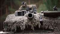 Es ist das Hauptwaffensystem des Leopard 2A6 abgebildet. Unscharf im Hintergrund ist Oberfeldwebel S. zu sehen
