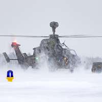 Ein Hubschrauber steht mit drehendem Rotor auf einer verschneiten Landebahn.