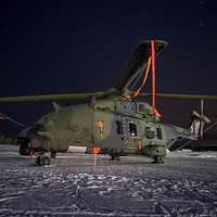 Nachtaufnahme: Ein Hubschrauber steht mit Abdeckplanen auf einem verschneiten Landeplatz.
