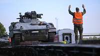 Auf einem Wagon weist ein Soldat einen Panzer in Position ein