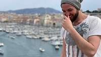 Ein Mann im Vordergrund. Im Hintergrund ist ein Hafen