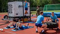 Fünf Rekruten in blauen Sportanzügen trainieren auf dem Sportplatz.